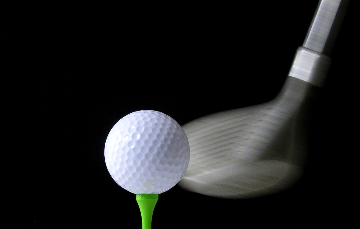 Mustalla pohjalla vihreän tiin päällä golfpallo