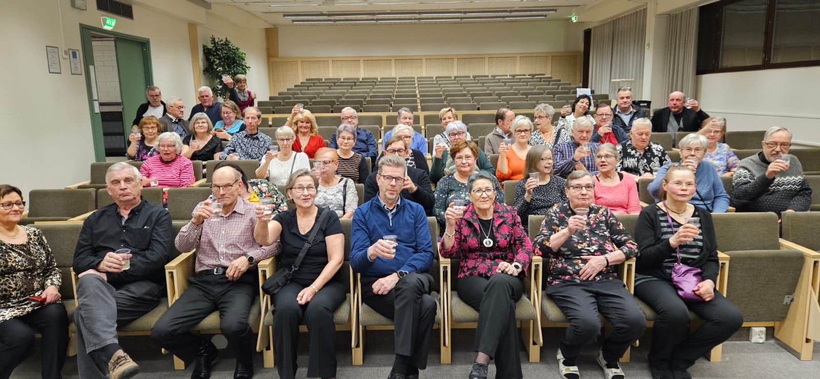Auditoriossa istuu ryhmä ihmisiä kuohuviinilasit käsissään