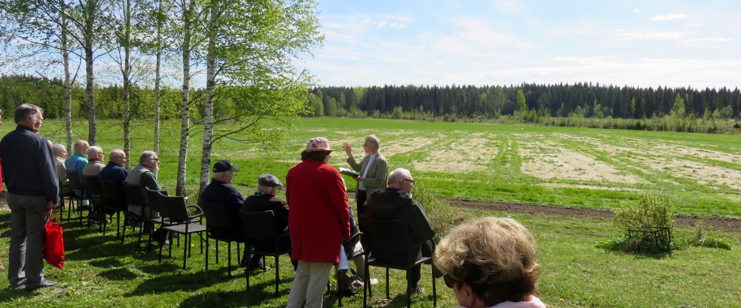 Väkeä istumassa aukean pellon laidalla