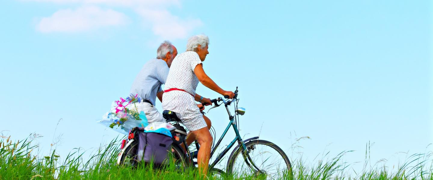 Kaksi vanhempaa ihmistä pyöräilee kesällä sinisen taivaan alla