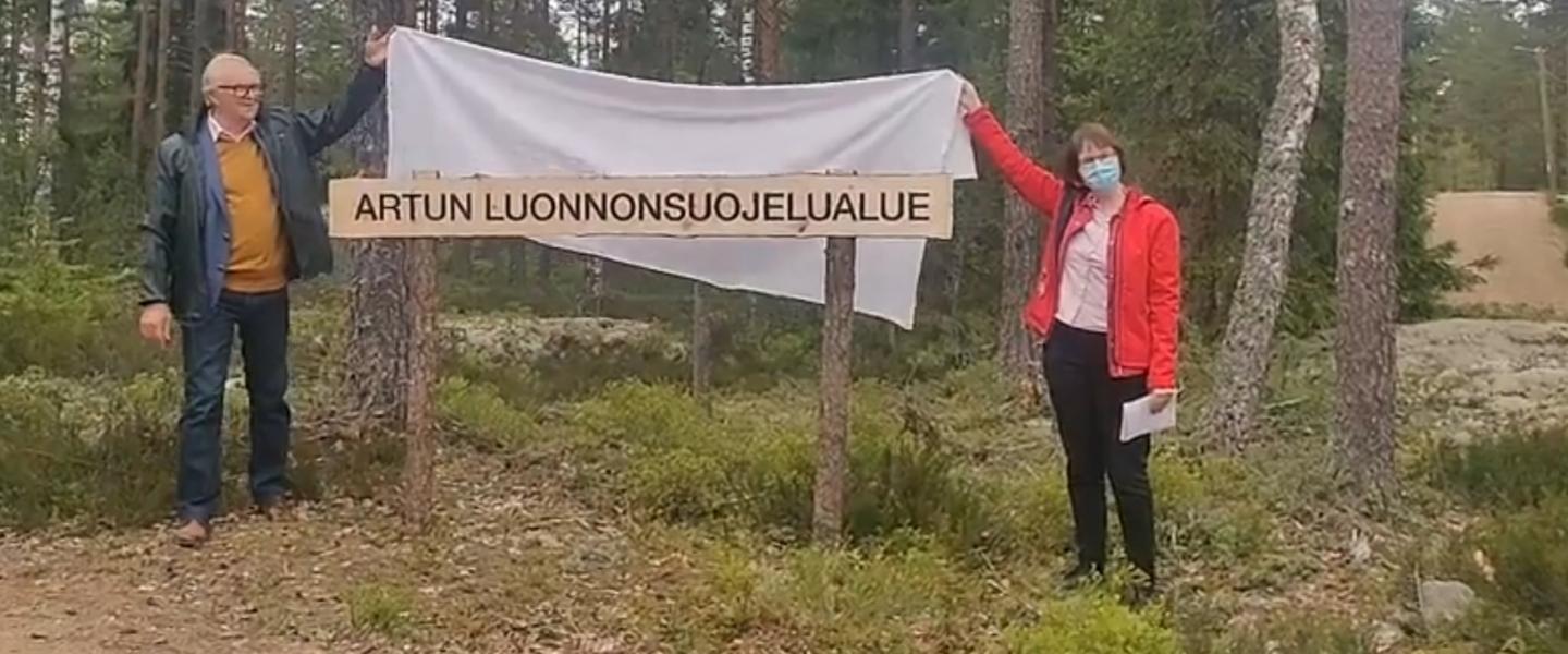 Eläkeliiton puheenjohtaja Raimo Ikonen ja Lehmirannan lomakeskuksen johtaja Tanja Bergroth nostavat lakanan pois luonnonsuojelualueen kyltin päältä metsän reunassa Salossa.