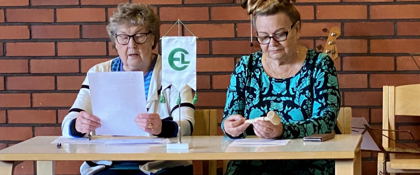 Eläkeliiton lippu ja puheenjohtaja ja sihteeri kokouspöydän ääressä