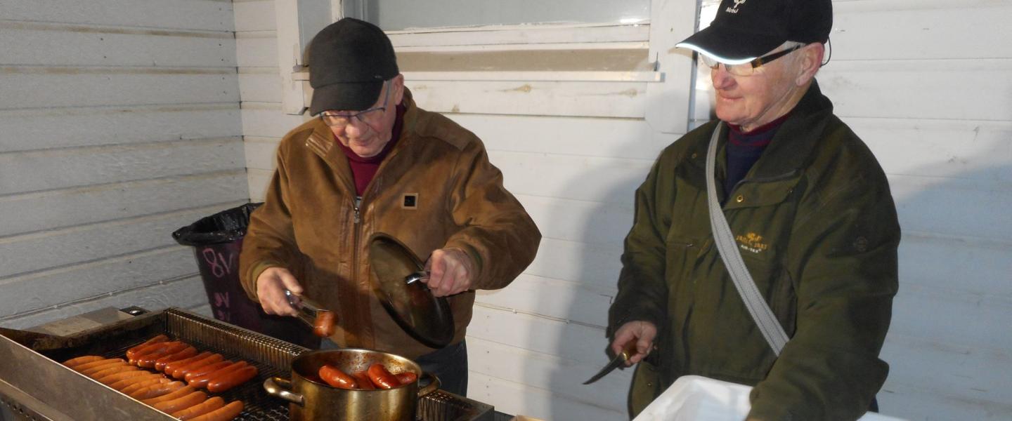 miehet paistavat grillillä makkaraa