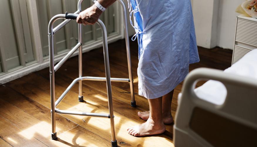 Vanhus nojaa kävelytukeen sairaalasängyn vieressä